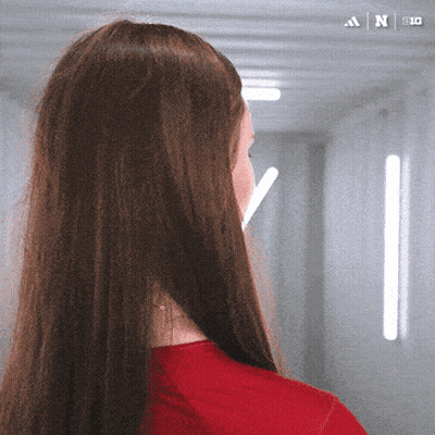 A Woman In A Red Shirt Is Standing In A Hallway With An Adidas Logo On The Bottom GIF