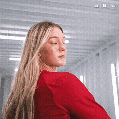 A Woman In A Red Shirt Is Standing In A Hallway With The Adidas Logo On The Bottom Left GIF