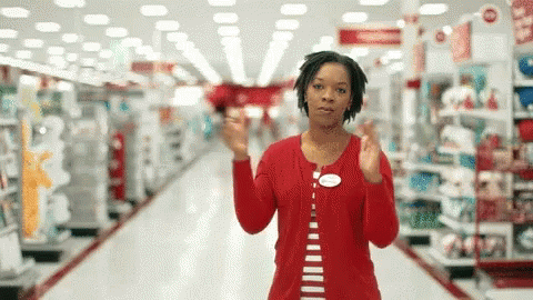 A Woman In A Red Shirt Is Standing In An Aisle Of A Store GIF