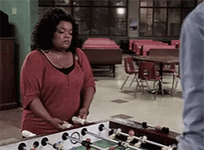 A Woman In A Red Shirt Is Standing In Front Of A Foosball Table GIF