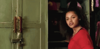 A Woman In A Red Shirt Is Standing In Front Of A Green Door With A Padlock On It . GIF