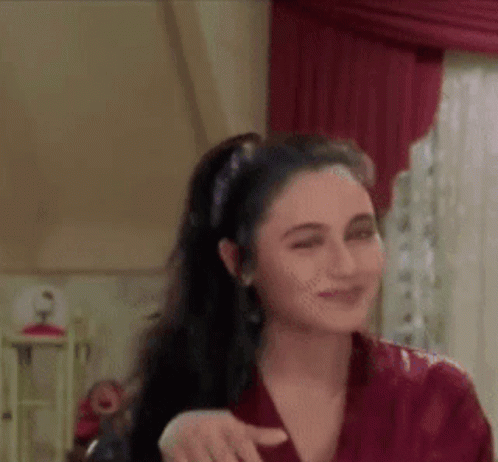 A Woman In A Red Shirt Is Standing In Front Of A Window In A Room . GIF