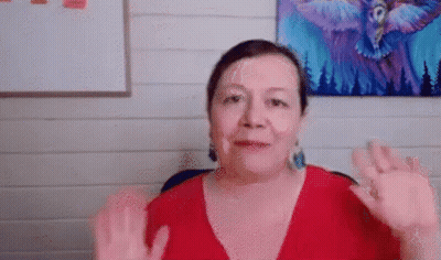 A Woman In A Red Shirt Is Waving Her Hands In Front Of A Painting Of An Owl . GIF