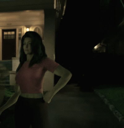 A Woman In A Red Shirt Stands In Front Of A House GIF