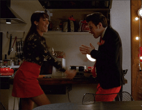 A Woman In A Red Skirt Is Standing Next To A Man In A Black Suit In A Kitchen GIF