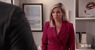 A Woman In A Red Suit Is Standing In Front Of A Netflix Box GIF