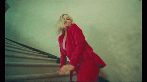 A Woman In A Red Suit Is Walking Down The Stairs GIF