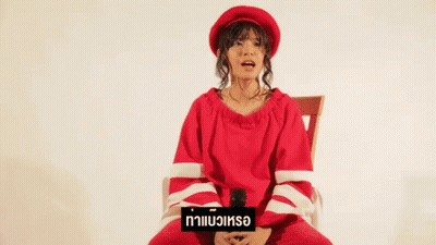 A Woman In A Red Sweater And Hat Is Sitting In A Chair Holding A Microphone . GIF
