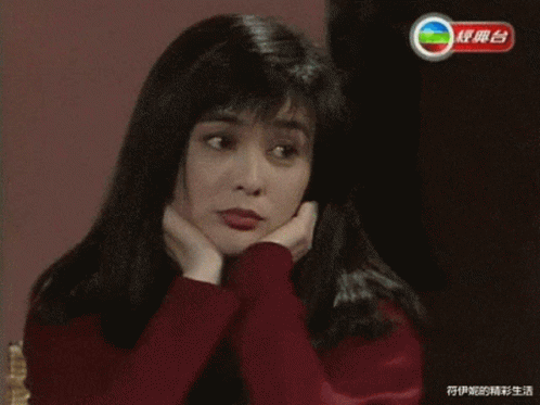 A Woman In A Red Sweater Has Her Hands On Her Face In Front Of A Tv Screen With Chinese Writing GIF