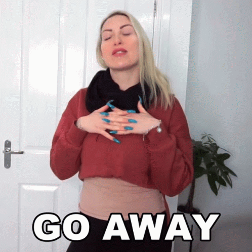 A Woman In A Red Sweater Holds Her Hands To Her Chest In Front Of A Sign That Says Go Away GIF
