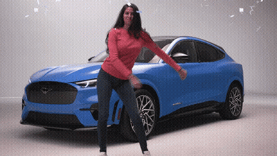 A Woman In A Red Sweater Is Dancing In Front Of A Blue Mustang GIF