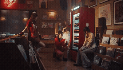A Woman In A Red Sweater Is Holding A Bottle Of Coca Cola In Front Of A Refrigerator . GIF
