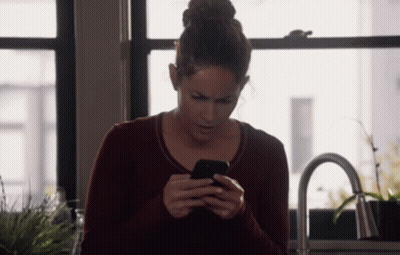 A Woman In A Red Sweater Is Looking At Her Phone GIF