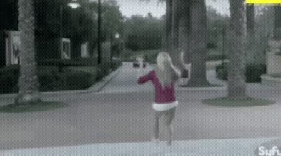 A Woman In A Red Sweater Is Running Down A Sidewalk . GIF
