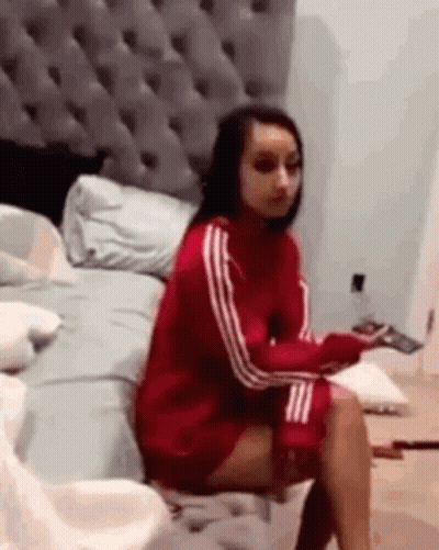 A Woman In A Red Sweater Is Sitting On A Bed . GIF