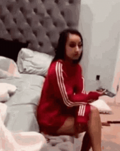 A Woman In A Red Sweater Is Sitting On A Bed With Her Legs Crossed . GIF