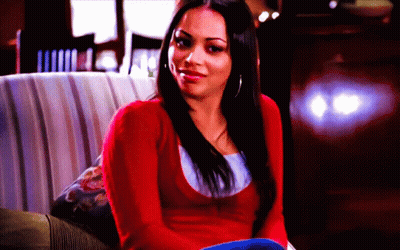 A Woman In A Red Sweater Is Sitting On A Couch And Smiling GIF