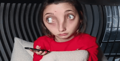 A Woman In A Red Sweater Is Sitting On A Couch Holding A Cell Phone And Making A Funny Face . GIF