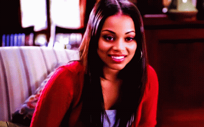 A Woman In A Red Sweater Is Smiling And Looking At The Camera GIF
