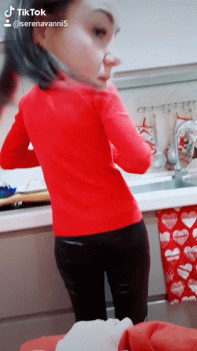 A Woman In A Red Sweater Is Standing In Front Of A Kitchen Sink With Hearts On It GIF