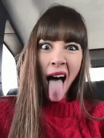 A Woman In A Red Sweater Is Sticking Her Tongue Out In A Car . GIF