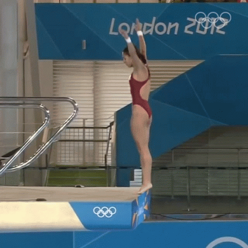 A Woman In A Red Swimsuit Is Jumping Off A Diving Board In Front Of A London 2012 Sign GIF