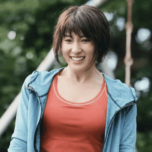 A Woman In A Red Tank Top And A Blue Jacket Smiles For The Camera GIF