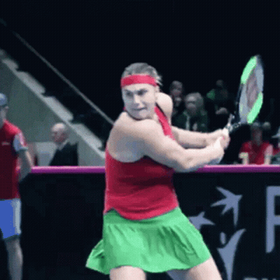 A Woman In A Red Tank Top And Green Skirt Is Swinging A Tennis Racket GIF