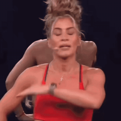 A Woman In A Red Tank Top Is Dancing With A Man In A Blue Shirt Behind Her . GIF