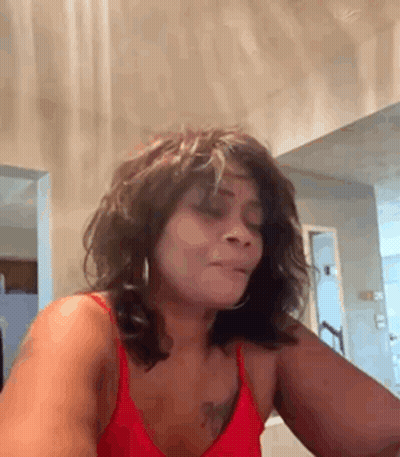 A Woman In A Red Tank Top Is Sitting In Front Of A Mirror . GIF