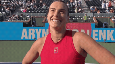 A Woman In A Red Tank Top Is Smiling In Front Of A Banner That Says " Aryn " GIF