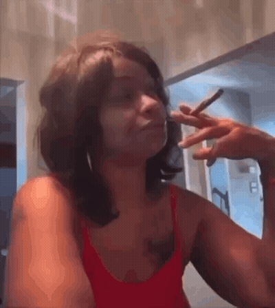 A Woman In A Red Tank Top Is Smoking A Cigarette In A Bathroom . GIF