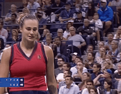 A Woman In A Red Tank Top Is Standing In Front Of A Crowd At A Tennis Game . GIF