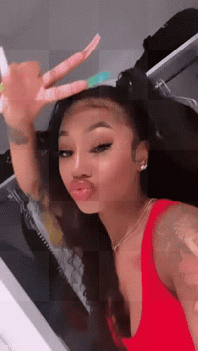 A Woman In A Red Tank Top Is Taking A Selfie In A Mirror . GIF