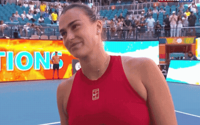 A Woman In A Red Tank Top Stands On A Tennis Court In Front Of A Sign That Says Tion GIF