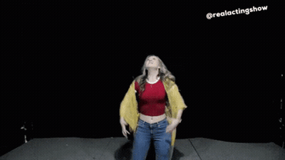 A Woman In A Red Top And A Yellow Jacket Is Dancing On A Stage With Her Arms In The Air . GIF