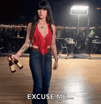 A Woman In A Red Top And Blue Jeans Is Holding Two Bottles Of Wine And Says Excuse Me GIF