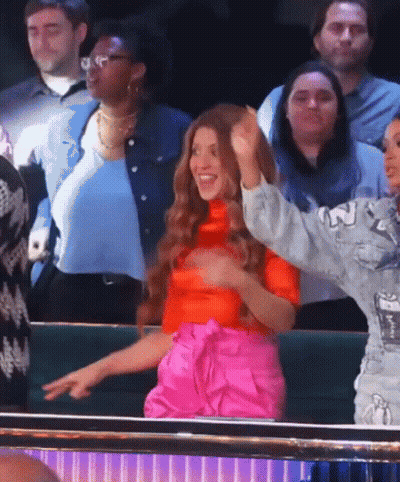 A Woman In A Red Top And Pink Pants Stands In A Crowd Of People GIF