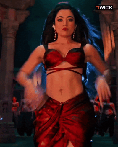 A Woman In A Red Top And Skirt Is Dancing In Front Of A Wick Logo GIF