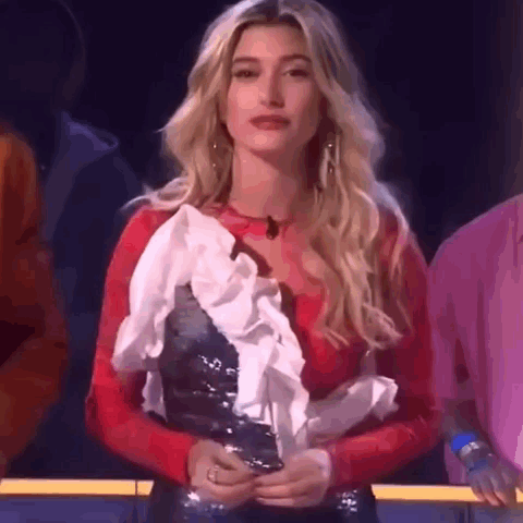 A Woman In A Red Top And White Ruffled Skirt Is Standing In Front Of A Crowd . GIF
