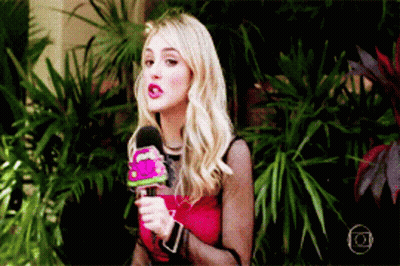 A Woman In A Red Top Is Holding A Microphone In Front Of Plants GIF