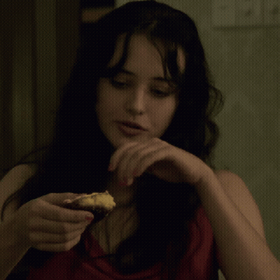 A Woman In A Red Top Is Holding A Piece Of Food In Her Hand GIF