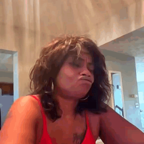 A Woman In A Red Top Is Making A Funny Face While Sitting At A Table . GIF