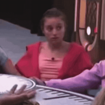 A Woman In A Red Top Is Sitting At A Table With A Clock On It . GIF