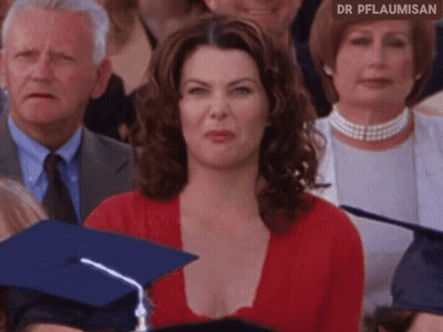 A Woman In A Red Top Is Sitting In A Crowd Of People With A Graduation Cap On . GIF