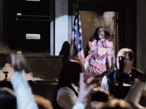A Woman In A Red White And Blue Dress Stands In Front Of A Flag GIF
