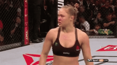 A Woman In A Reebok Bra Is Standing In A Cage During A Ufc Fight . GIF
