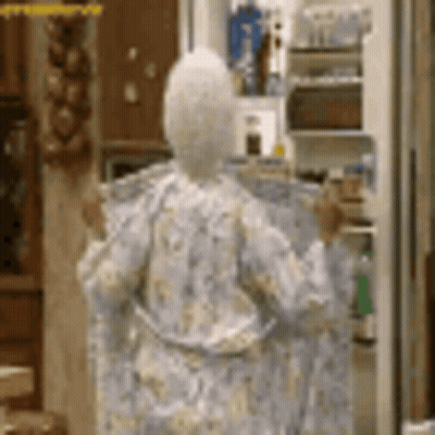 A Woman In A Robe Is Standing In Front Of A Refrigerator In A Kitchen . GIF