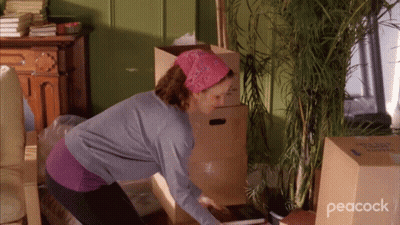 A Woman In A Room With Boxes And A Peacock Logo On The Bottom Right GIF