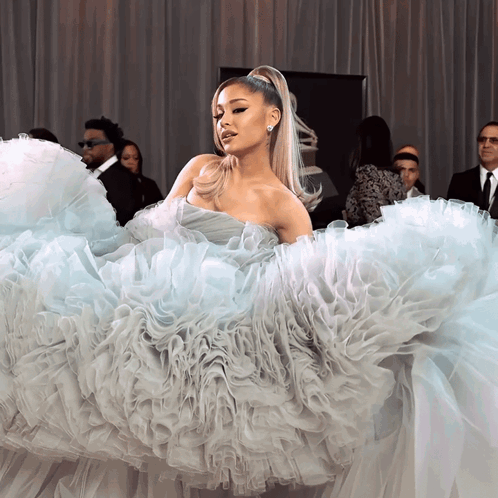 A Woman In A Ruffled Dress Stands In Front Of A Group Of Men GIF